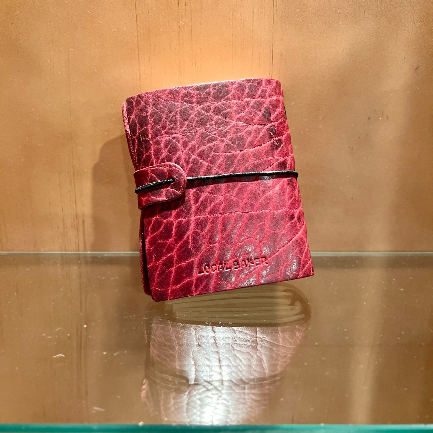 Red leather wallet with 'Locals Only' branding on a reflective surface.