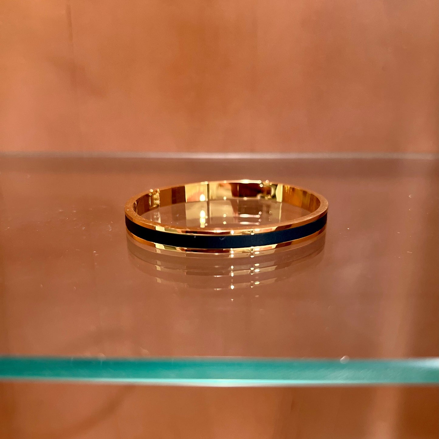 Gold bracelet with a black band on a glass shelf against a brown background
