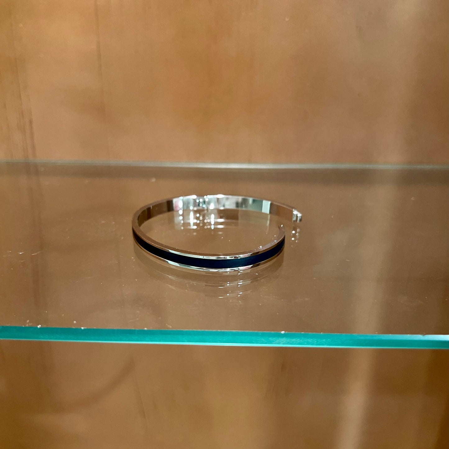 Silver bracelet on a glass shelf with a wooden background