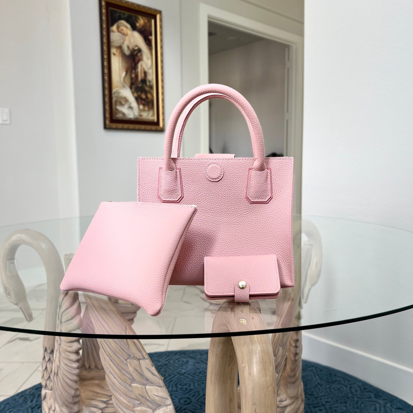 Pink handbag and wallet set on a decorative table with a painting in the background