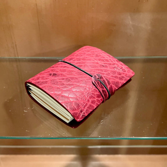 Pink textured notebook on a glass shelf against a wooden wall