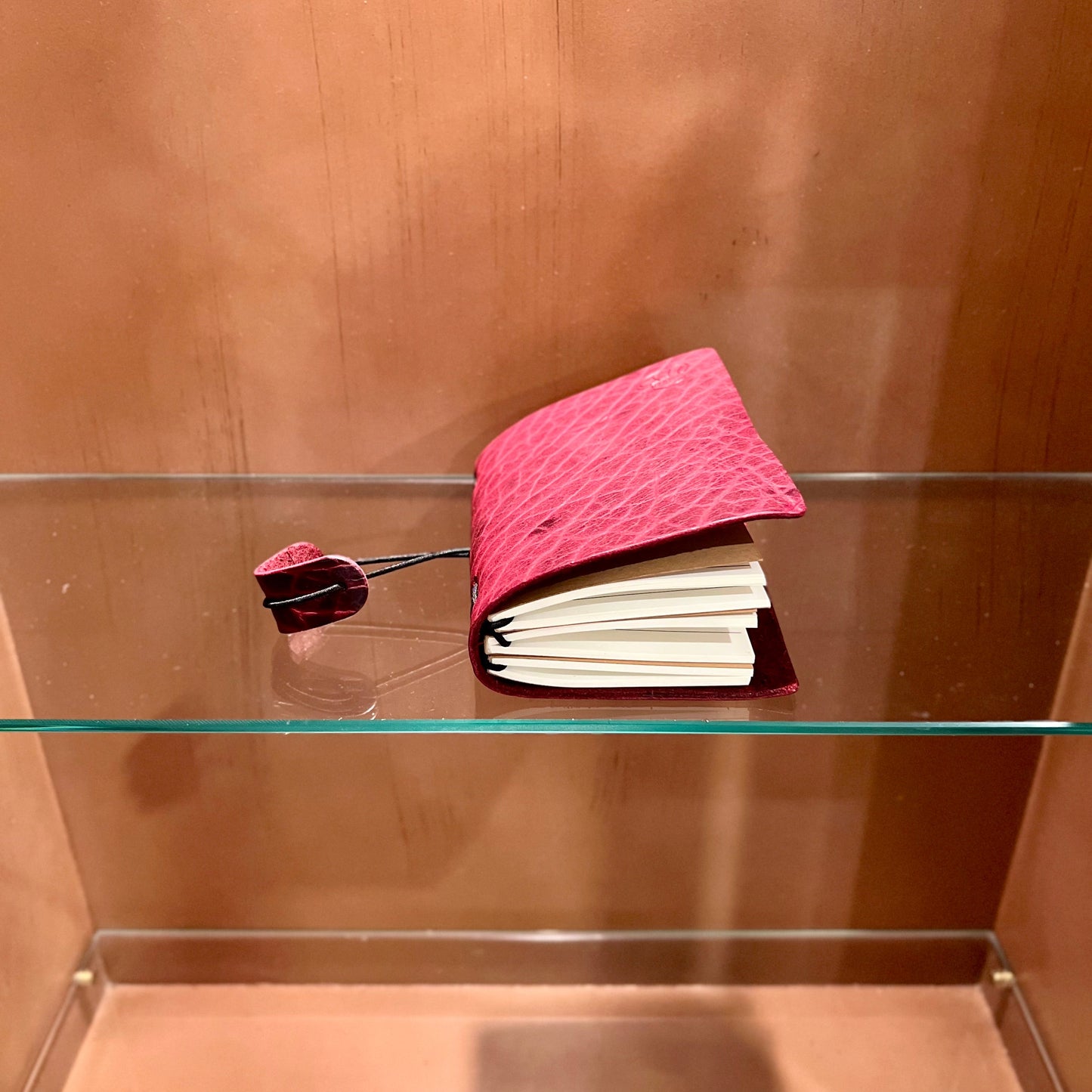 Pink textured book on a glass shelf with a wooden background
