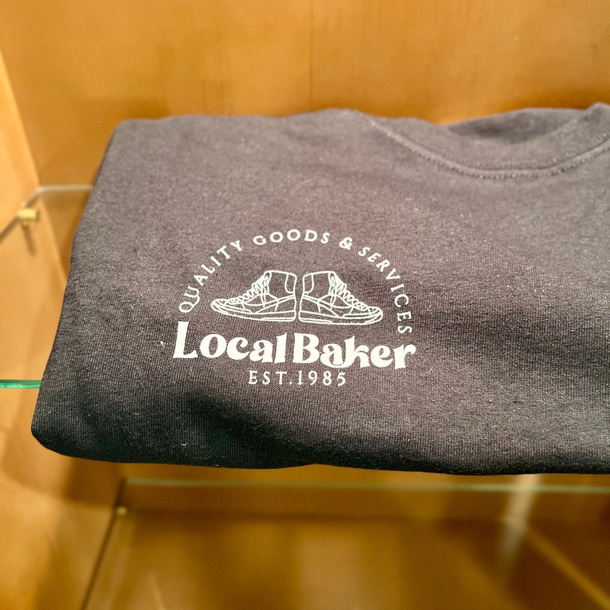 Folded gray t-shirt with 'Local Baker' logo on a wooden surface
