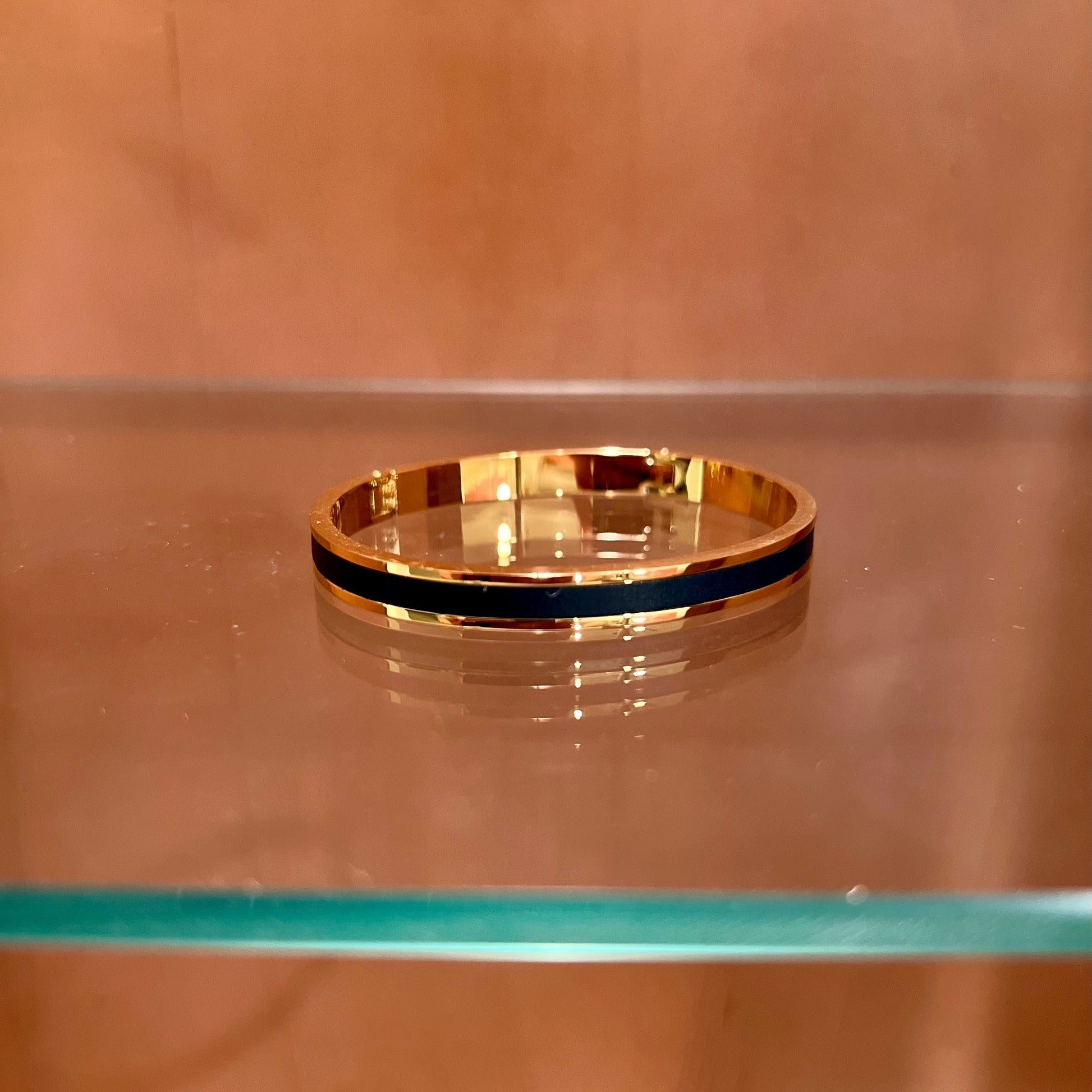 Gold bracelet with a black band on a glass shelf against a brown background