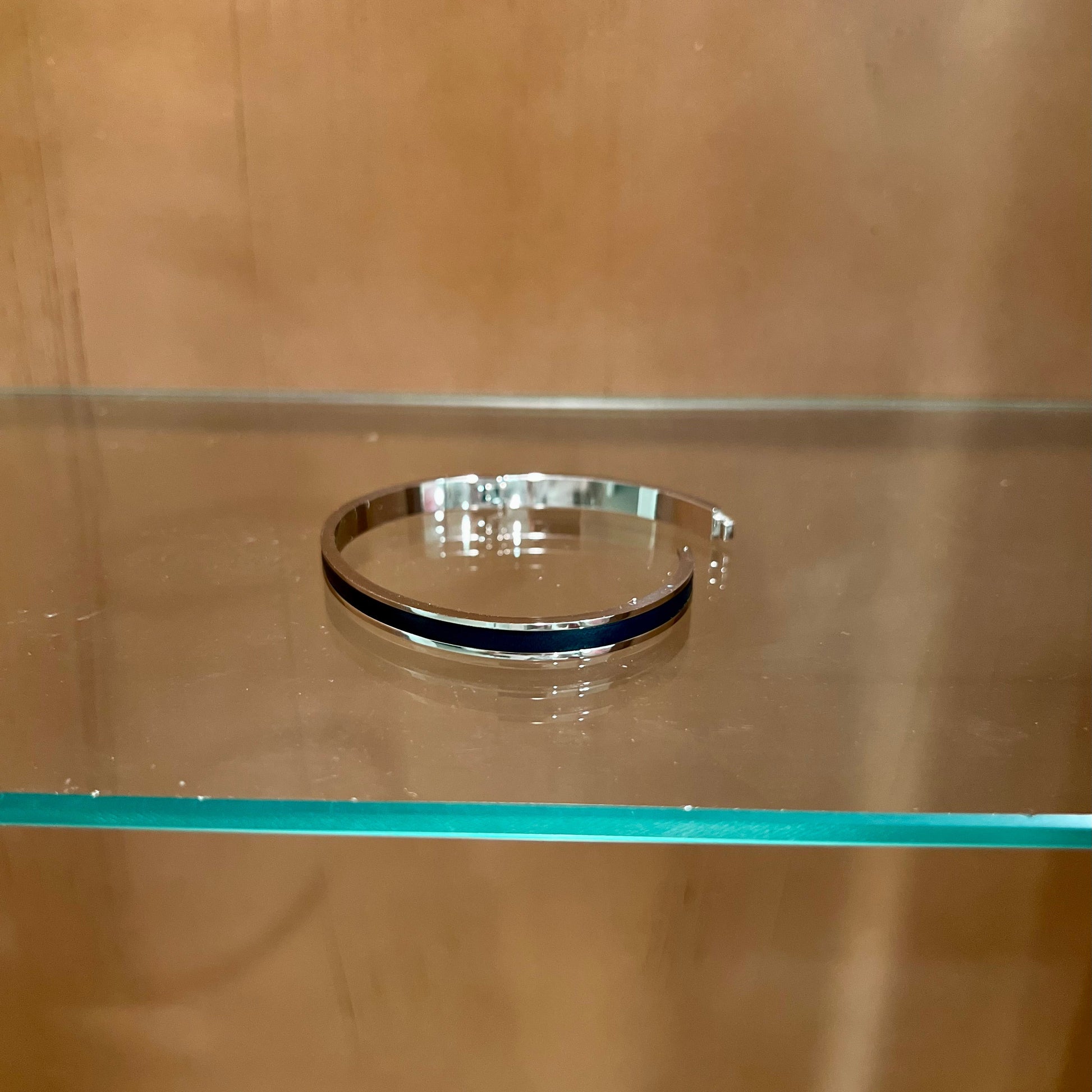 Silver bracelet on a glass shelf with a wooden background