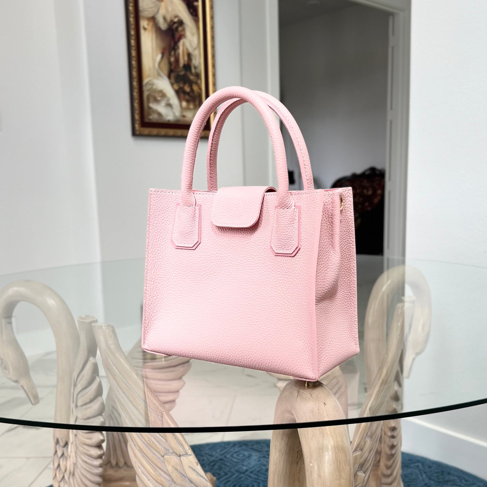 Pink handbag on a decorative stand with a painting in the background